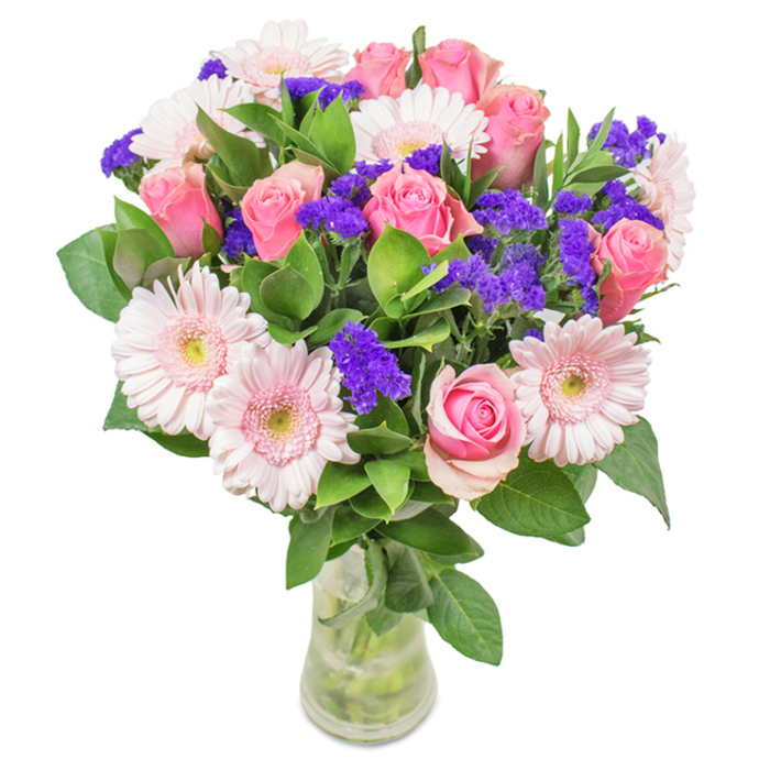 Set against a crisp white background, this vibrant bouquet from Florist Limehouse draws the eye to its artful arrangement of roughly seven to nine medium and soft pink roses-each one at a different stage of bloom, from tightly wound bud to newly unfurled spiral. Complementing the roses are five to seven pale pink gerbera daisies, easily recognised by their wide, round faces and almost-white, textured centres. Across the bouquet, vivid purple clusters of statice provide a lively counterpoint, offering texture and further depth. A base of rich, hunter green foliage cradles the blooms, its abundant leaves giving the whole arrangement a feeling of freshness, akin to wandering through neighbouring King Edward Memorial Park. The bouquet's clear glass vase reveals fresh-cut stems and clear water, echoing the purity and honesty of local Limehouse floristry. With its balanced tones of pink and purple and layers of greens, the bouquet is perfectly suited as a gift for anniversaries, birthdays, Mother's Day, or simply to add an uplifting touch to a home or office overlooking the canal. Every detail is meticulously crafted by expert hands, ensuring this bouquet is both a feast for the senses and a welcome gesture of joy and affection.